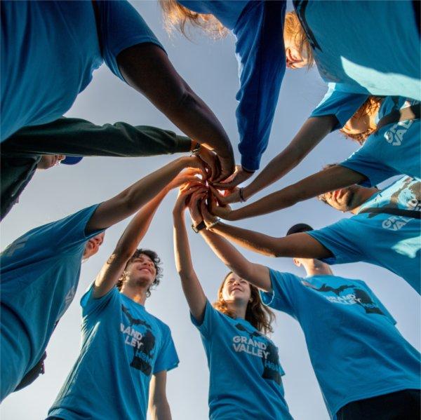 A group of RAs wearing matching blue shirts put their hands together in a circle formation.