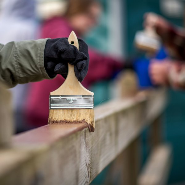 Student applies paint to a wooden fence at Muskegon State Park