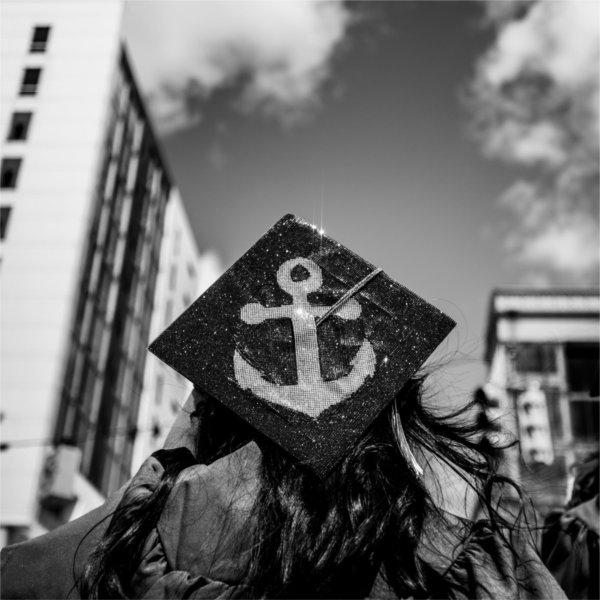 A graduate holds a bedazzled graduation cap with the GV Athletics logo.